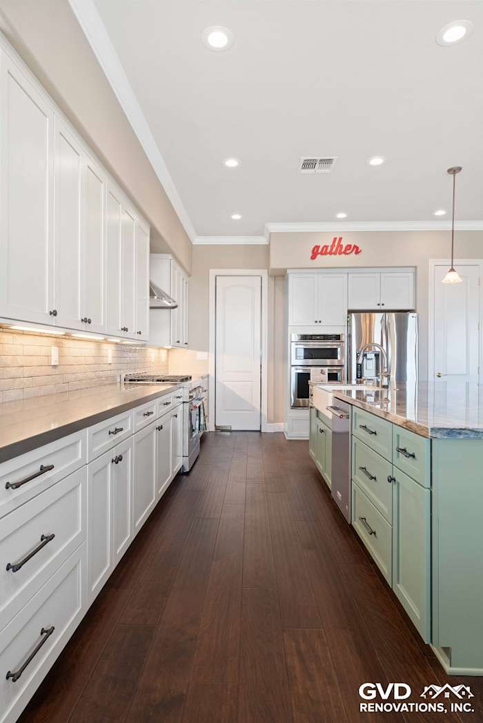 Spacious kitchen featuring white cabinetry, green island, stainless steel appliances, and elegant wood flooring