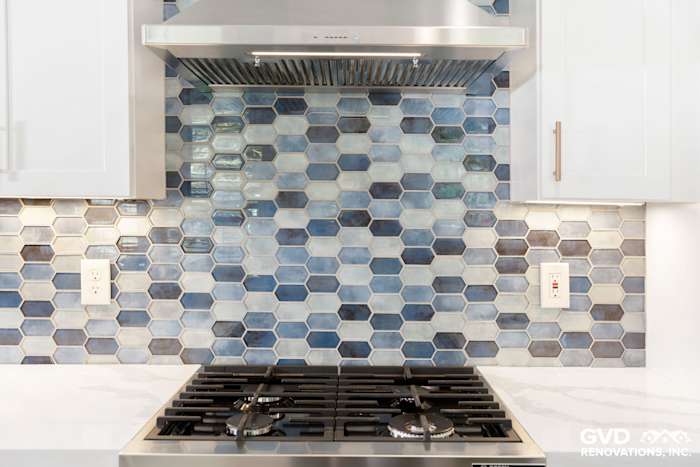 Hexagon tile backsplash in shades of blue, modern gas stove, and stainless steel hood in remodeled Sacramento kitchen