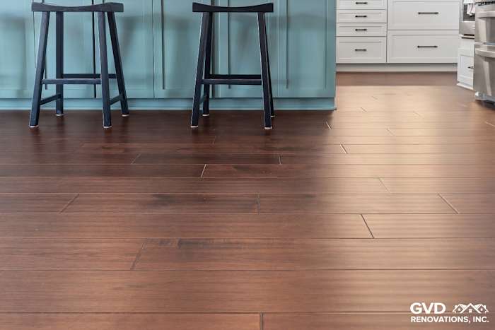 Dark hardwood flooring with a sleek finish, two black stools, and light blue cabinetry in a renovated kitchen