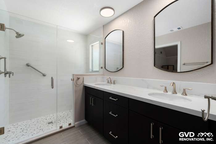 Modern master bathroom with dual sinks, dark cabinetry, round mirrors, and a glass shower