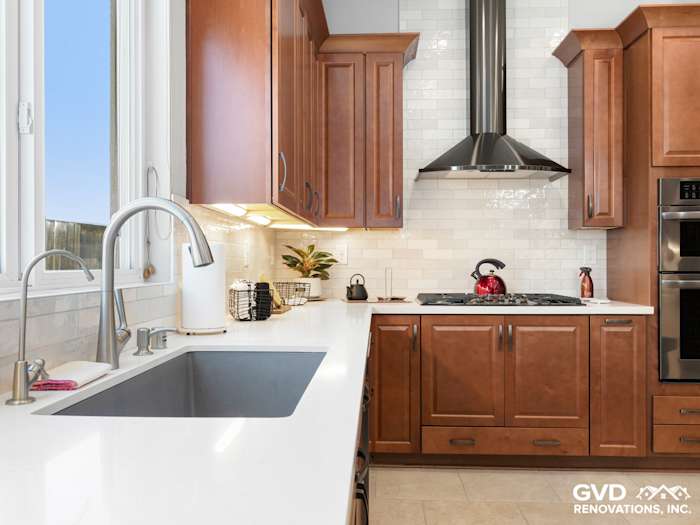 Modern kitchen with dark wood cabinets, white quartz countertops, and a stainless steel hood above the stove