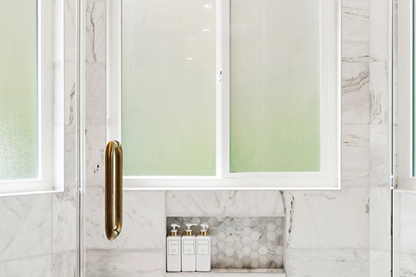 Expansive walk-in shower with marble tiles, gold fixtures, and clear glass enclosure in a master bathroom remodel