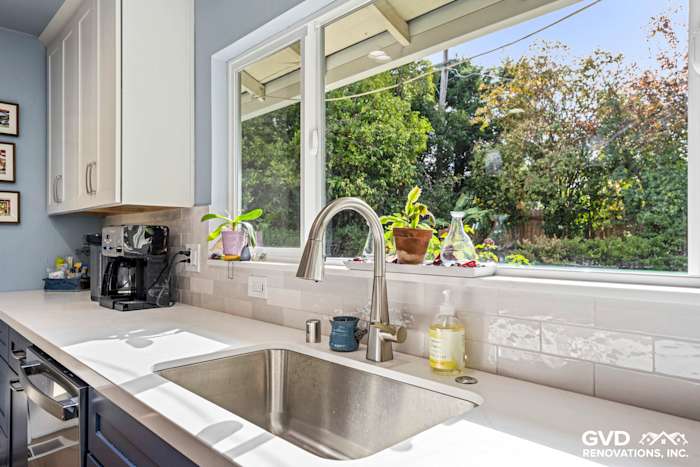 Modern kitchen sink with stainless steel bowl, quartz countertop, and large window overlooking greenery in Fair Oaks