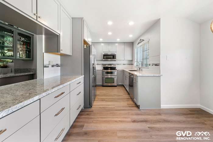 Modern kitchen remodel featuring gray cabinetry, granite countertops, stainless steel appliances, and wood-like flooring
