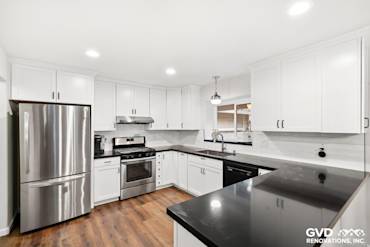 Modern kitchen featuring white cabinetry, black countertops, stainless steel appliances, and hardwood flooring