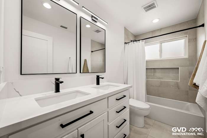 Modern bathroom featuring dual vanity with black fixtures, white cabinets, and tub/shower combo in Antelope home
