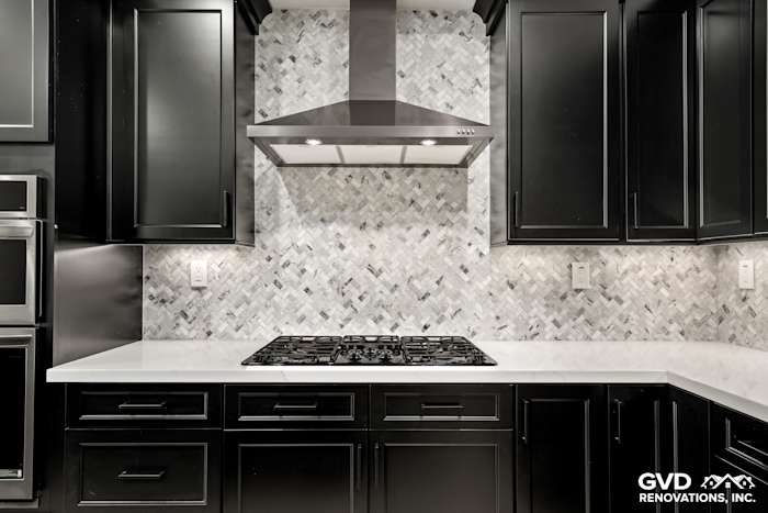 Stylish kitchen with black Waypoint cabinets, MSI herringbone backsplash, and quartz countertops featuring a custom mitered