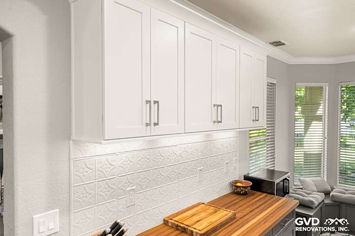 Modern white kitchen cabinets with chrome handles above a wood countertop and textured backsplash in Folsom remodel