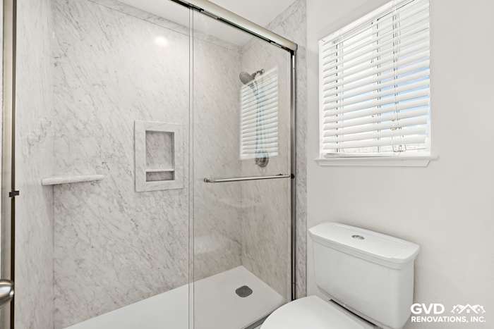 Modern walk-in shower with marble walls, built-in niche, and sleek glass door in remodeled Sacramento bathroom