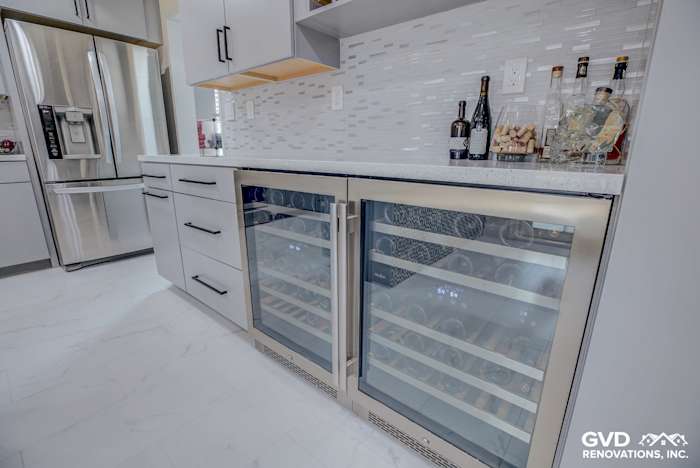 Modern kitchen with dual wine coolers, white cabinets, gray backsplash, and granite countertop