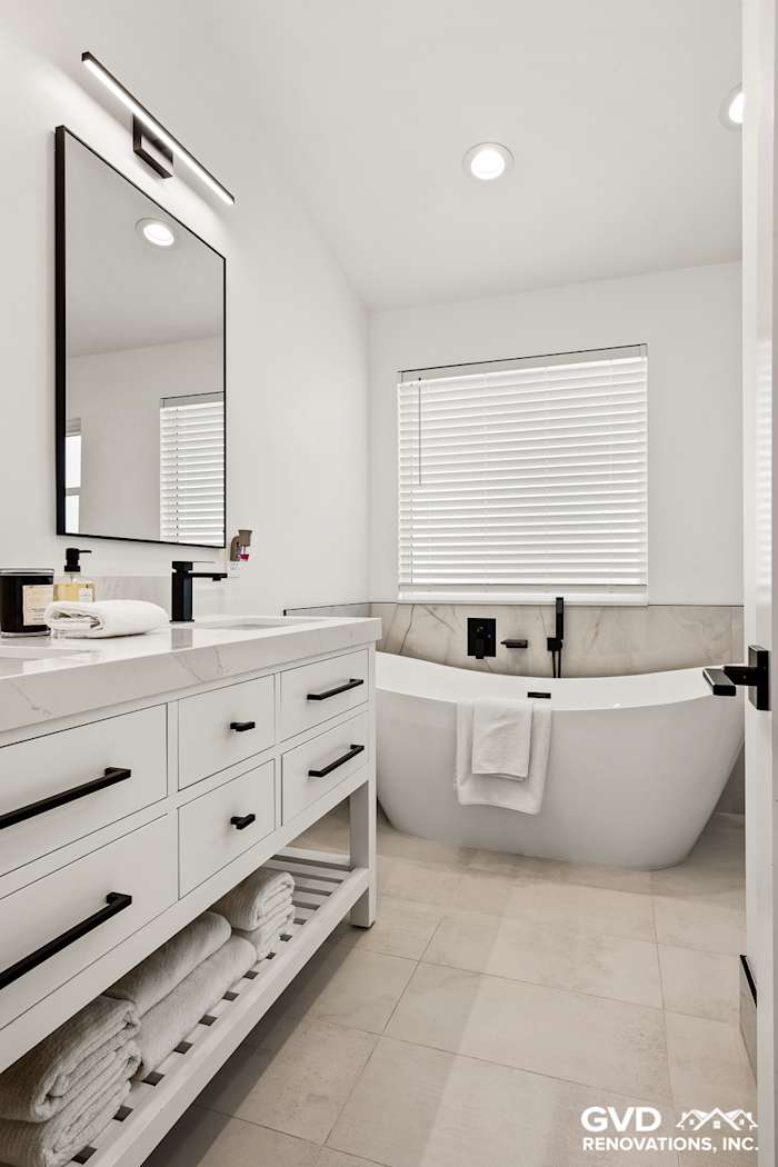 Modern bathroom featuring a freestanding tub, dual vanity, and large mirror with bright lighting
