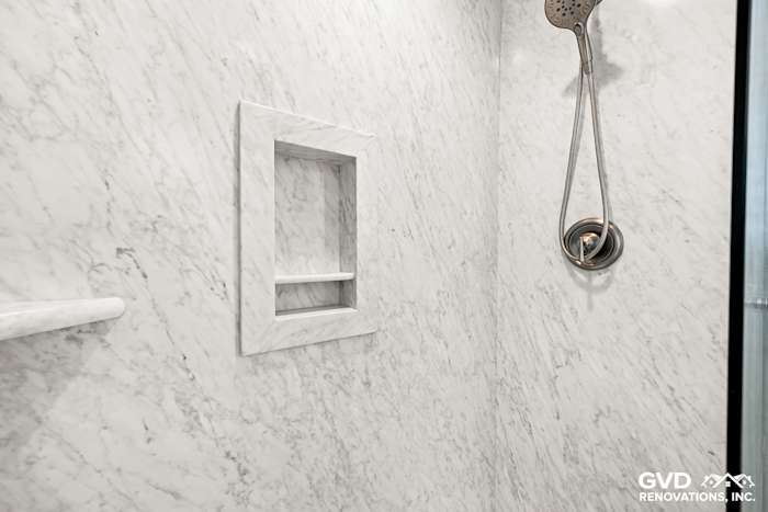 Modern walk-in shower featuring marble walls, built-in shelf, and sleek showerhead in remodeled bathroom