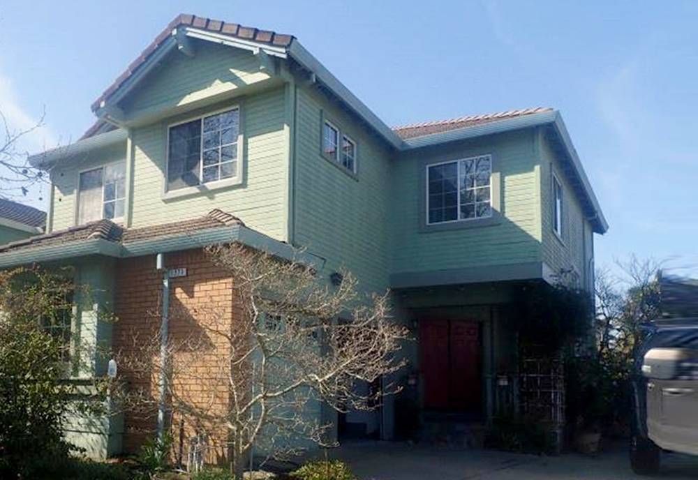 Worn green siding with brick accents on a two-story home