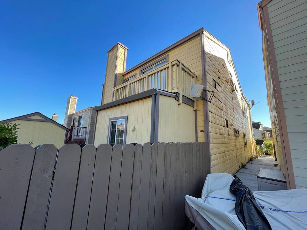 Multistory Sacramento home with yellow siding, fenced yard, and blue sky overhead