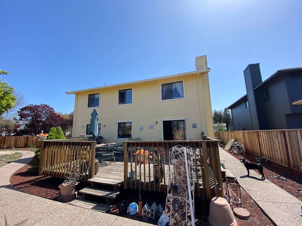 Wide view of a yellow two-story home with wooden deck and landscaped yard in Sacramento