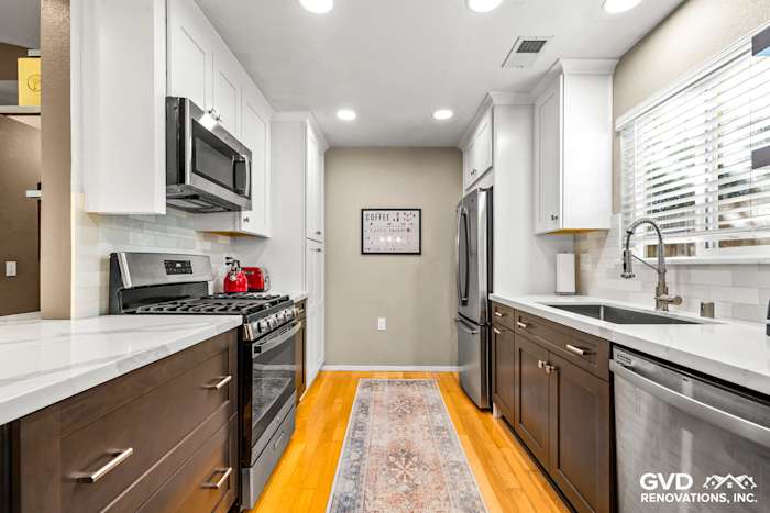 Modern kitchen in Davis featuring white and dark cabinets, quartz countertops, stainless steel appliances, and a runner rug