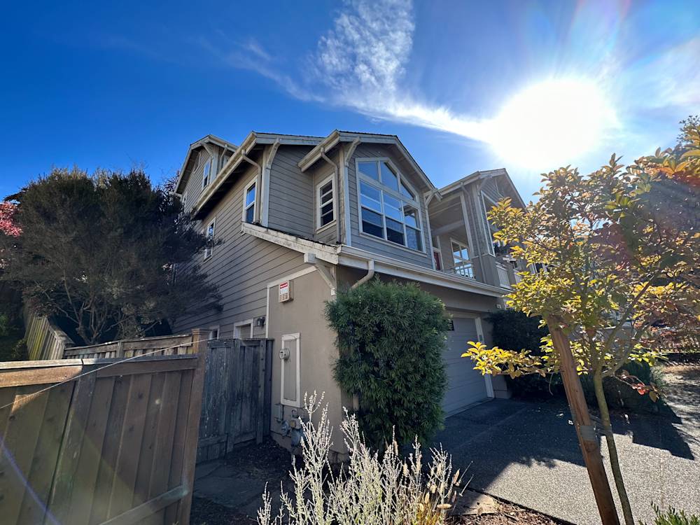 Two-story home exterior in Madera with gray siding and landscaping, sunlit sky above