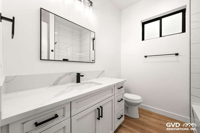 Modern bathroom with white cabinetry, marble countertop, large mirror, and black accents in new construction home