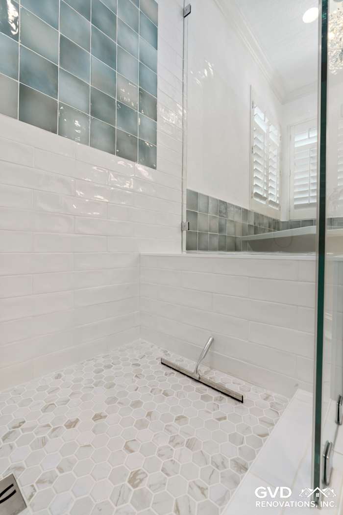 Modern bathroom with a glass shower, white hexagon floor tiles, and turquoise subway tiles on the walls