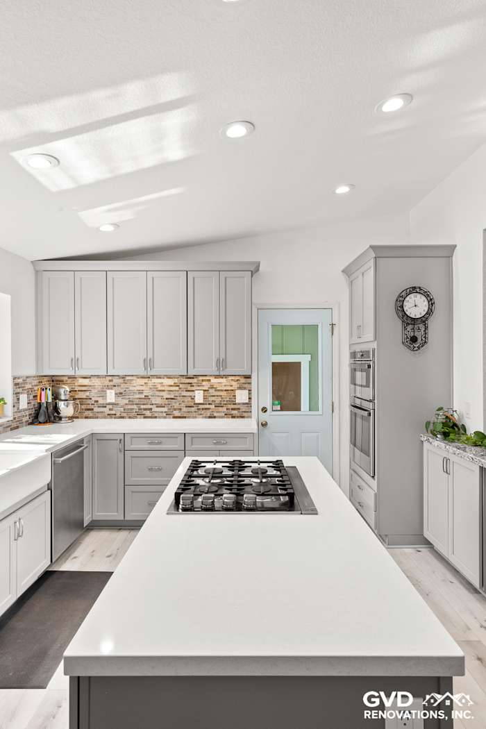 Modern kitchen remodel with gray cabinetry, white quartz island, and decorative stone backsplash in Greenwood, CA