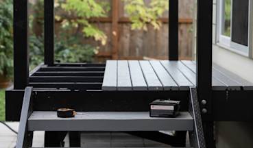 Modern outdoor deck under construction with gray wood planks, black frame, and tools visible in Sacramento backyard