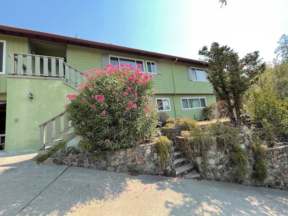 Exterior view of a Sacramento home with green walls and stone landscaping, featuring vibrant pink flowers