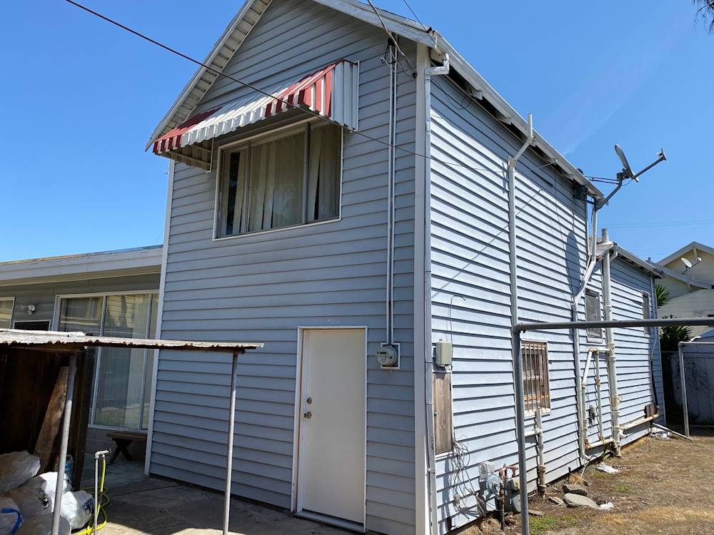 Old blue siding on a Sacramento home, featuring a striped awning and utility lines