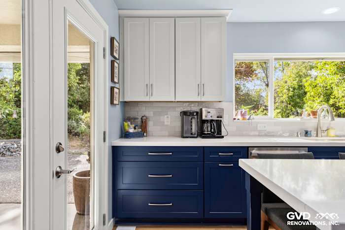 Modern kitchen corner with navy-blue cabinets, white quartz countertops, and natural light from large window
