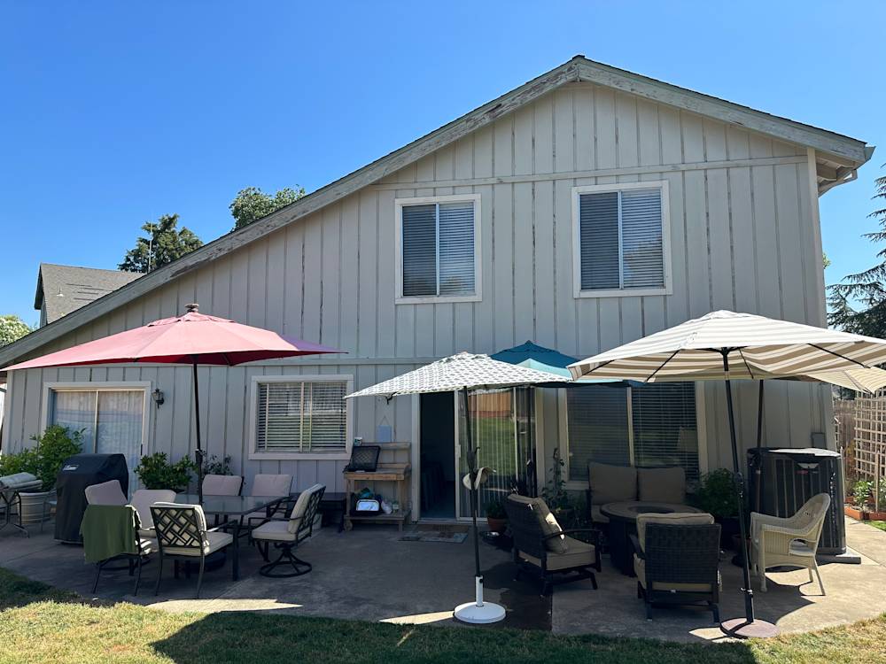Spacious backyard in Sacramento with patio furniture and sun umbrellas, featuring faded siding and greenery