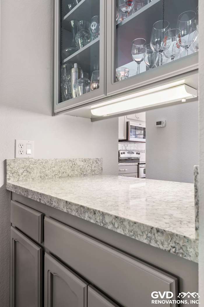 Elegant kitchen remodel in Carmichael featuring gray cabinets and a shimmering granite countertop with glassware display