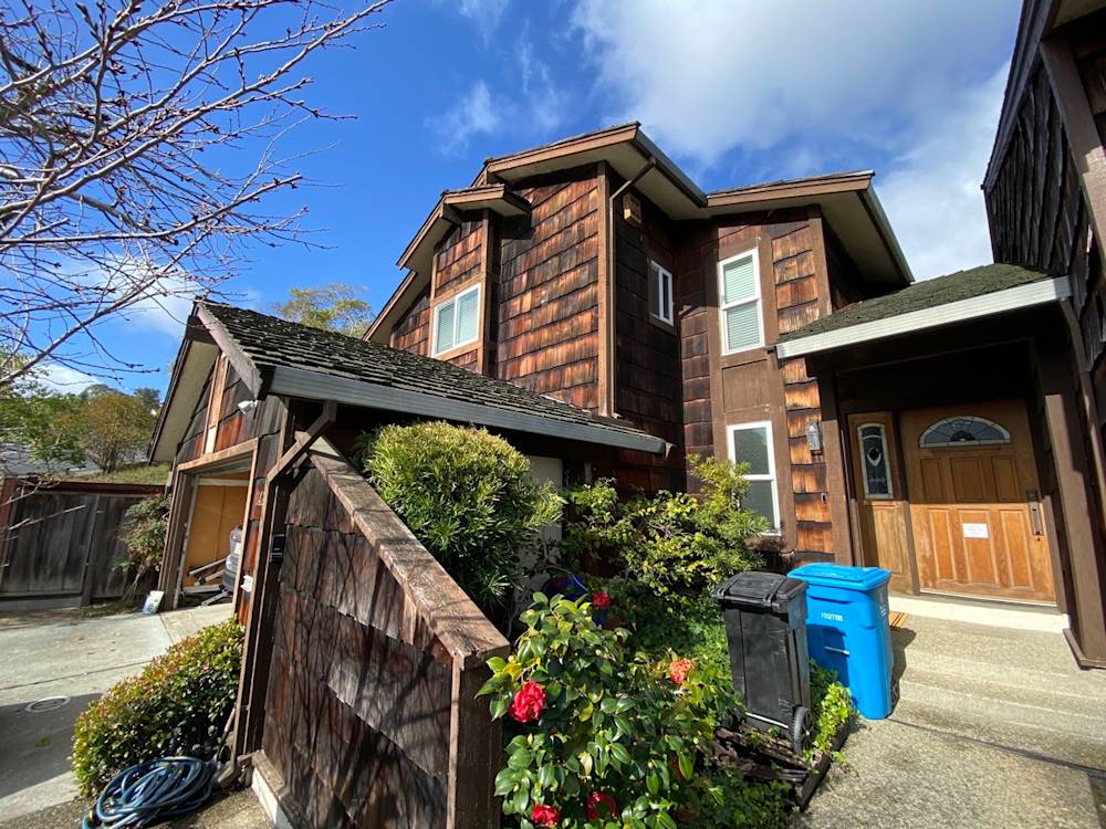 Wooden siding and landscaped entrance of a home in Sacramento, featuring shrubs and a colorful flower bed