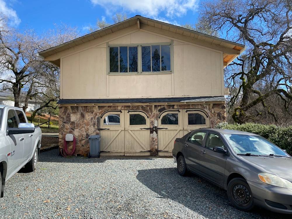 Stone and wood garage with large windows, surrounded by gravel and trees in Northern California