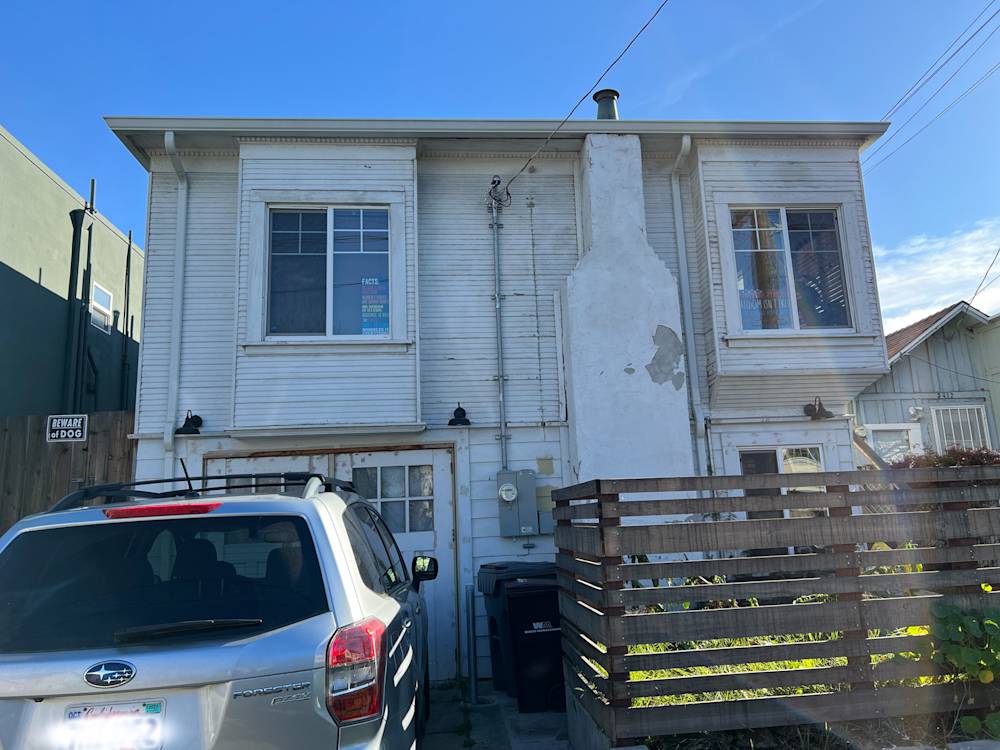 Two-story building with peeling white paint, visible chimney, and wooden fence in Oakland