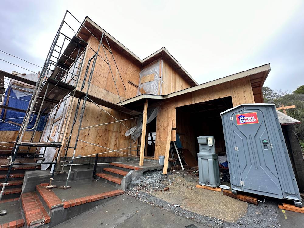 Unfinished house exterior in Tiburon, CA with scaffolding, exposed wood, and construction debris