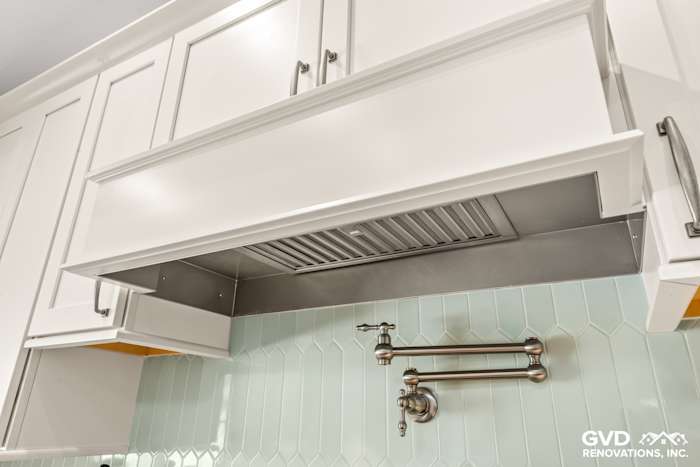 Custom white kitchen hood over a mint green backsplash with hexagonal tiles in Carmichael remodel