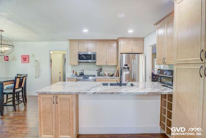 Modern kitchen with quartz countertops, light wood cabinets, and stainless steel appliances. Open layout design in Sacramento