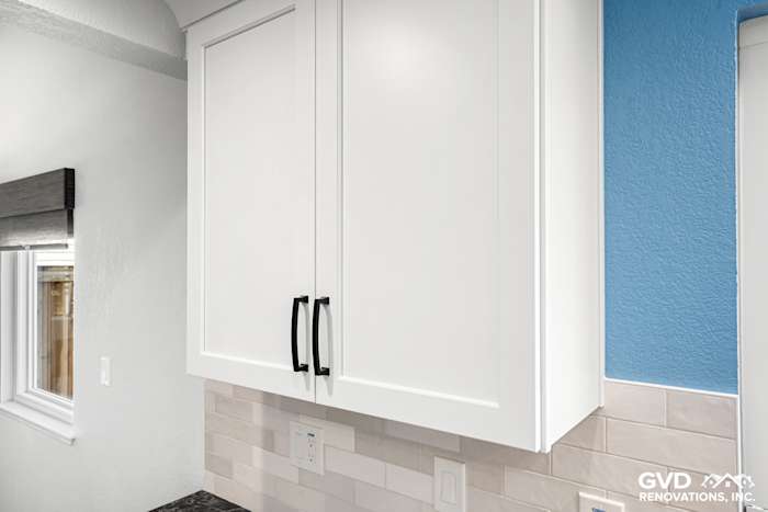 Modern kitchen cabinetry with sleek white doors, black handles, and blue accent wall in Fair Oaks, CA