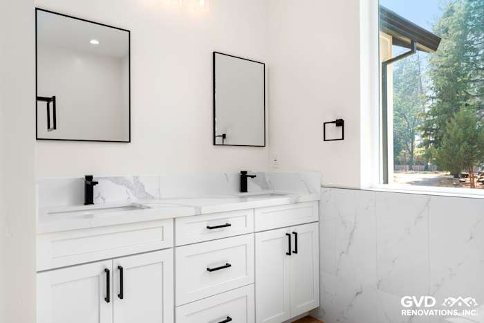 Spacious bathroom featuring white cabinetry, dual sinks, black fixtures, and marble wall accents in Paradise, CA