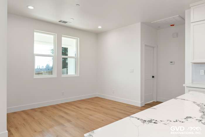 Bright interior kitchen space featuring white walls, large windows, and light wood flooring