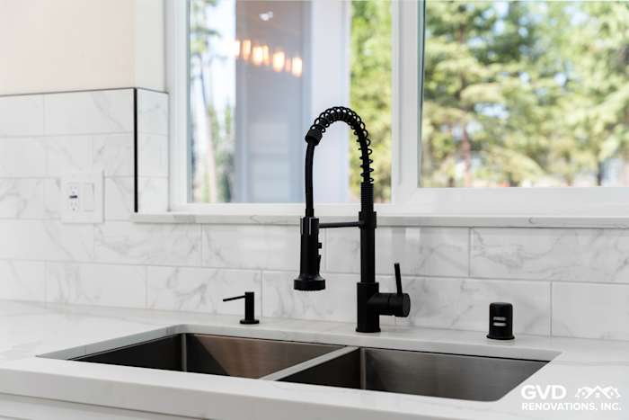 Modern kitchen sink featuring a black pull-down faucet and stainless steel double basin, accented by white marble backsplash