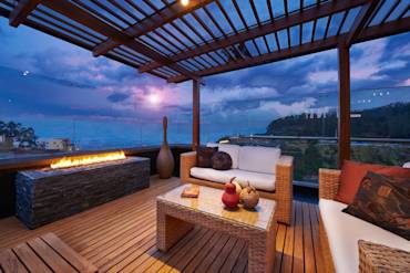 Stylish outdoor living space with wooden deck, modern furniture, and fire feature, showcasing serene sunset views