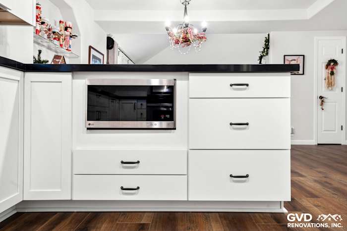 Modern white shaker kitchen island featuring black countertop, microwave, and ample storage drawers