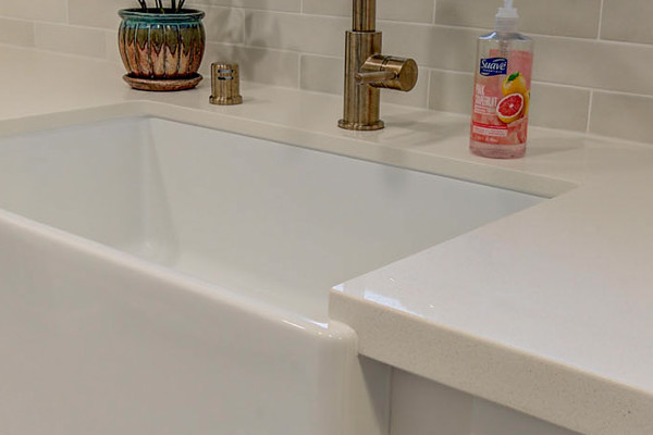 Farmhouse sink with gold faucet, white cabinetry, and herringbone tile backsplash in renovated Fair Oaks kitchen