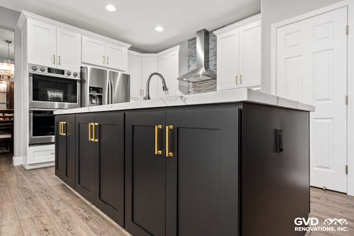 Modern kitchen remodel featuring a dark island with gold hardware, Cambria countertops, and white cabinets