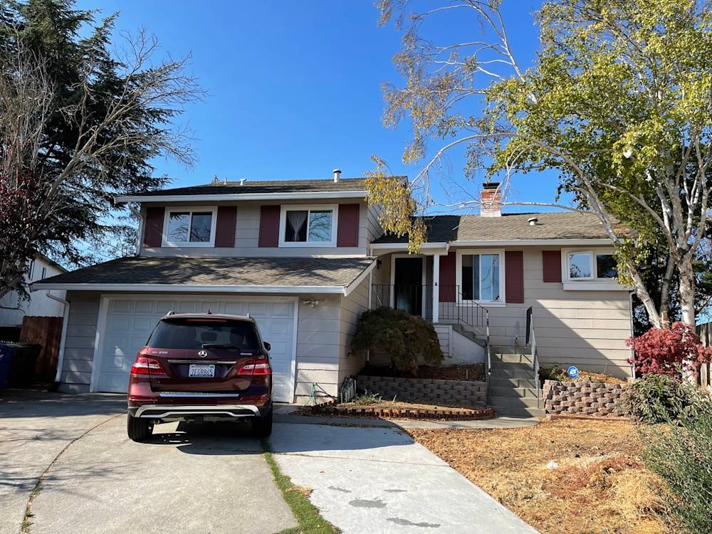 Two-story home in Sacramento with beige siding, red accents, and overgrown landscaping