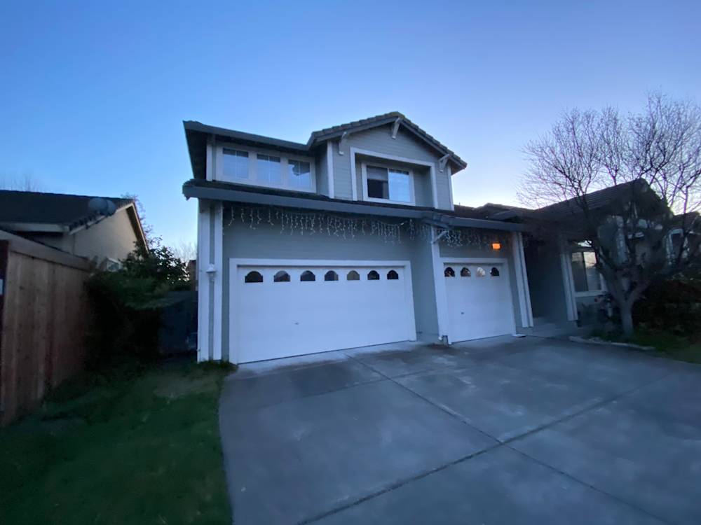 Two-story gray home with white garage doors and green lawn in Sacramento
