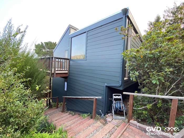 Dark blue James Hardie siding on home exterior with wooden deck and lush greenery in Mill Valley