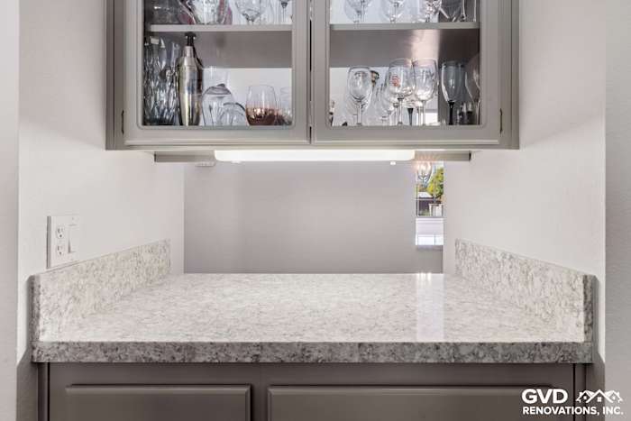 Gray cabinetry with glass doors and a sparkling white quartz countertop in a kitchen remodel