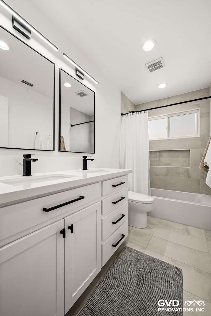Modern bathroom remodel featuring dual vanities, black fixtures, white cabinetry, and a sleek tub in Antelope, CA