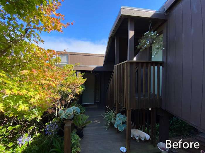 Before photo of home exterior featuring wooden deck, lush greenery, and unrenovated siding